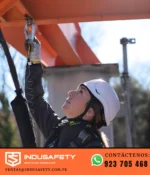 Trabajadora con casco de altura Granite Peak y arnés conectada a línea de vida en estructura metálica.